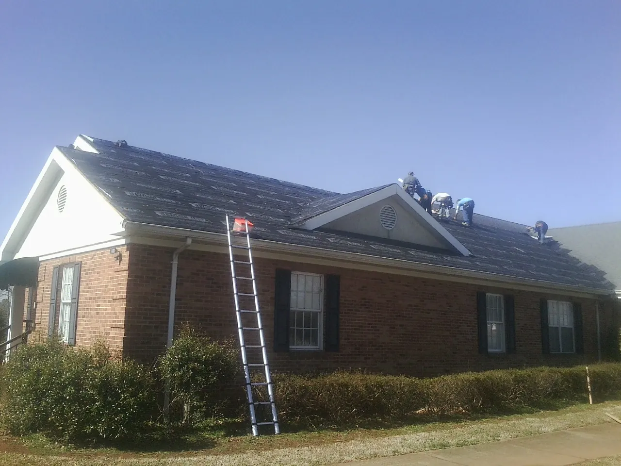 Crew tearing shingles off a brick ranch roof with a ladder set — Emergency Roof Repair work by our crew in Woosung