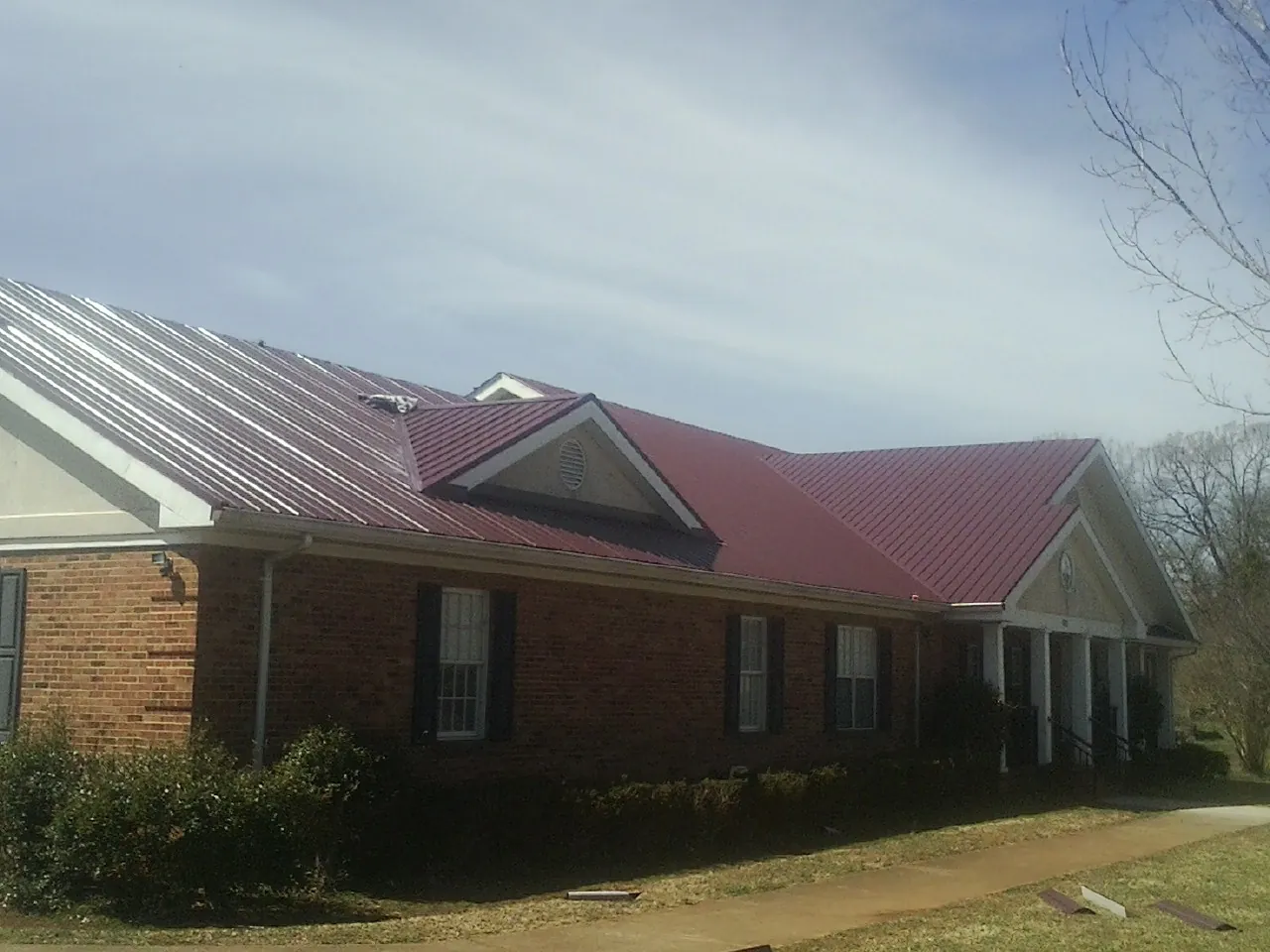 Red metal roof with gabled entries on a long brick building, from a Hail Damage Roof Repair job in Woosung