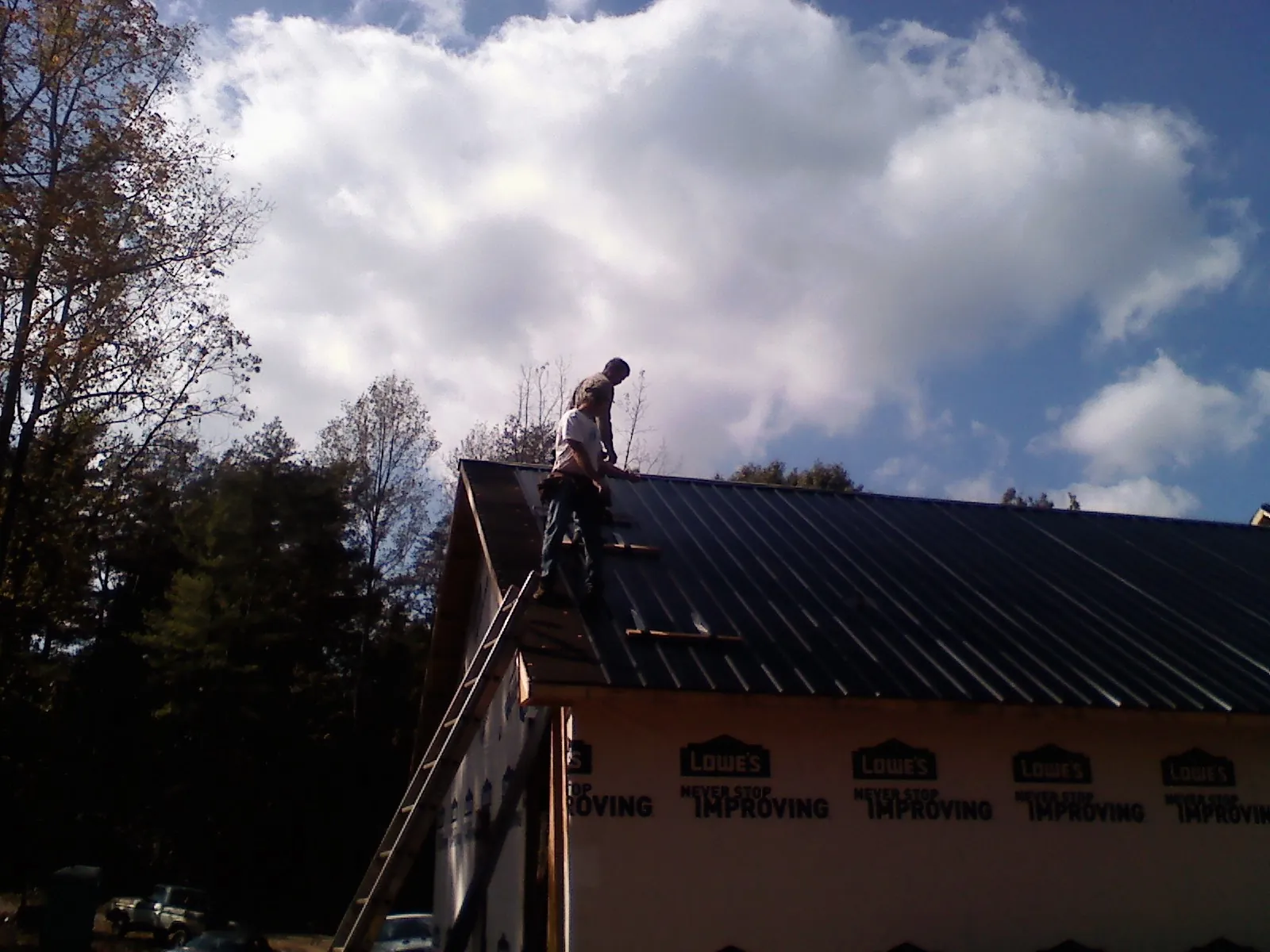 Roofer fastening dark metal panels high against a cloudy sky, from a Roof Inspection job in Woosung