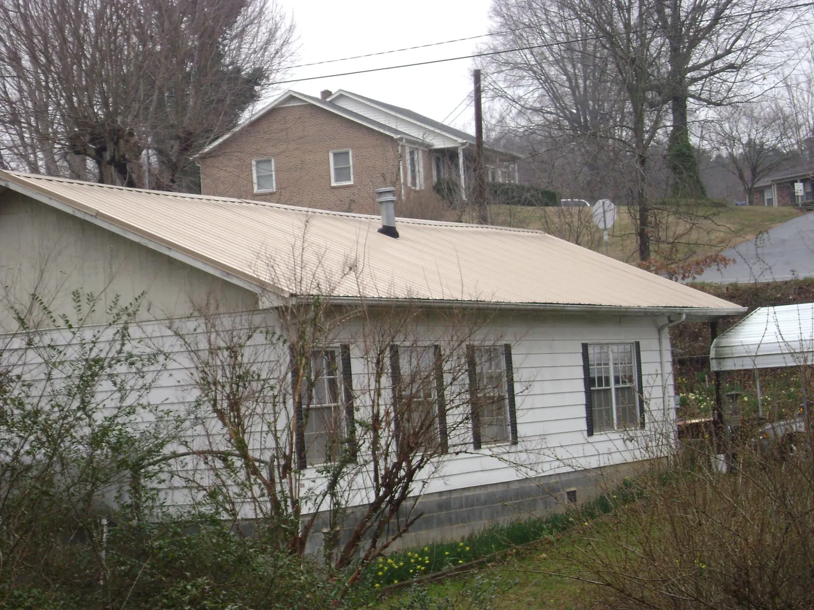 Tan metal roof on a white sided house set into a hillside — Commercial Roofing by Roofing Brothers in Woosung